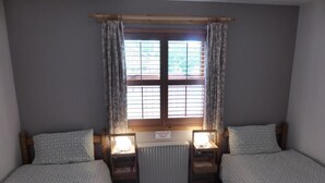Ein Schlafzimmer mit zwei Betten, einem Fenster mit Jalousien, einem Heizkörper und Nachttischlampen.