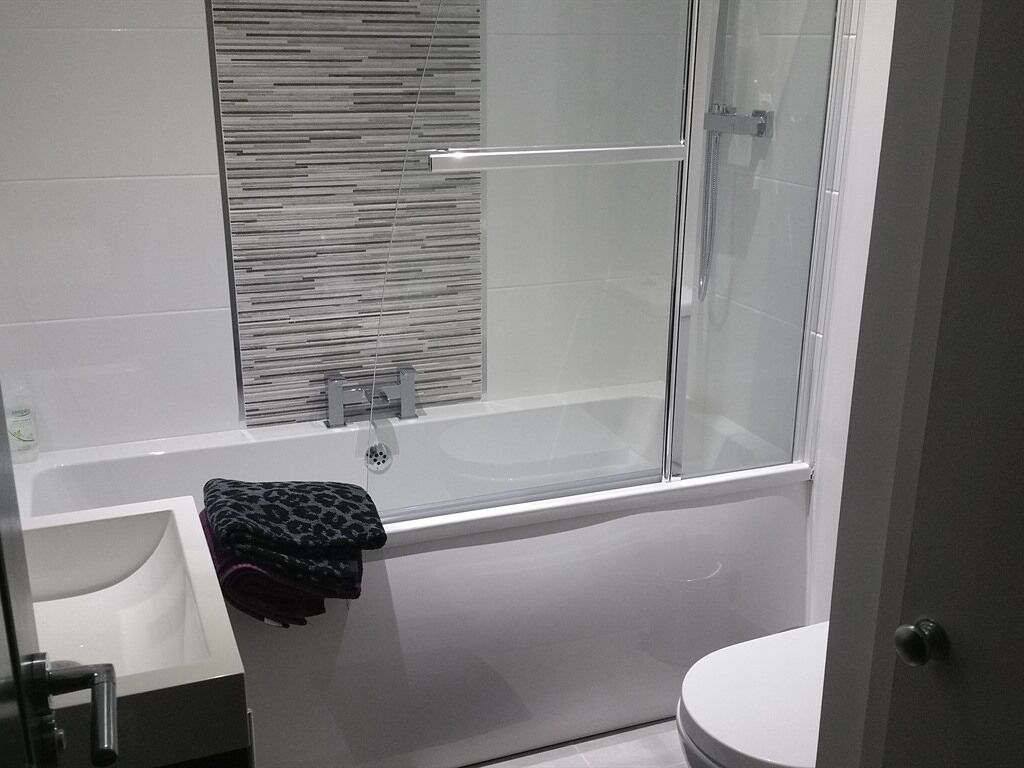 A modern bathroom with a glass-enclosed shower, a white bathtub, and a toilet.