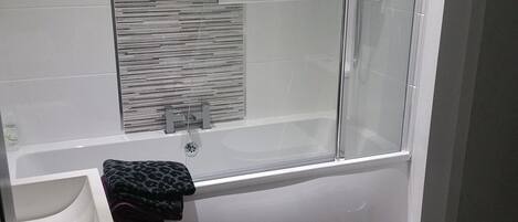 A modern bathroom with a glass-enclosed shower, a white bathtub, and a toilet.