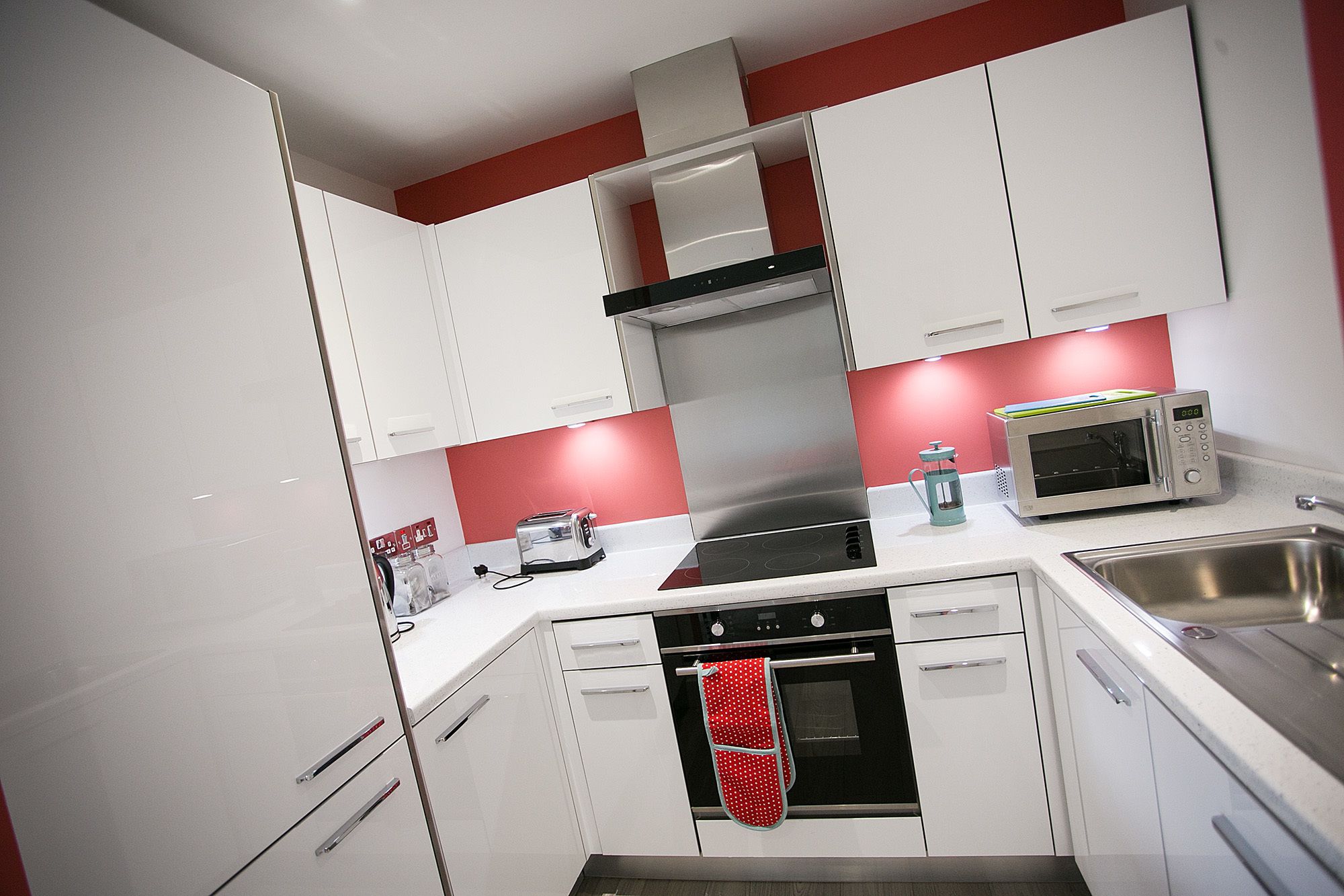 A modern kitchen with white cabinets, a stainless steel range hood, a microwave, and a built-in oven.