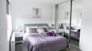 A modern bedroom with a large bed, bedside tables, a mirror, and artwork on the wall.