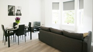 A modern living room with a sofa, dining table, chairs, and a TV.