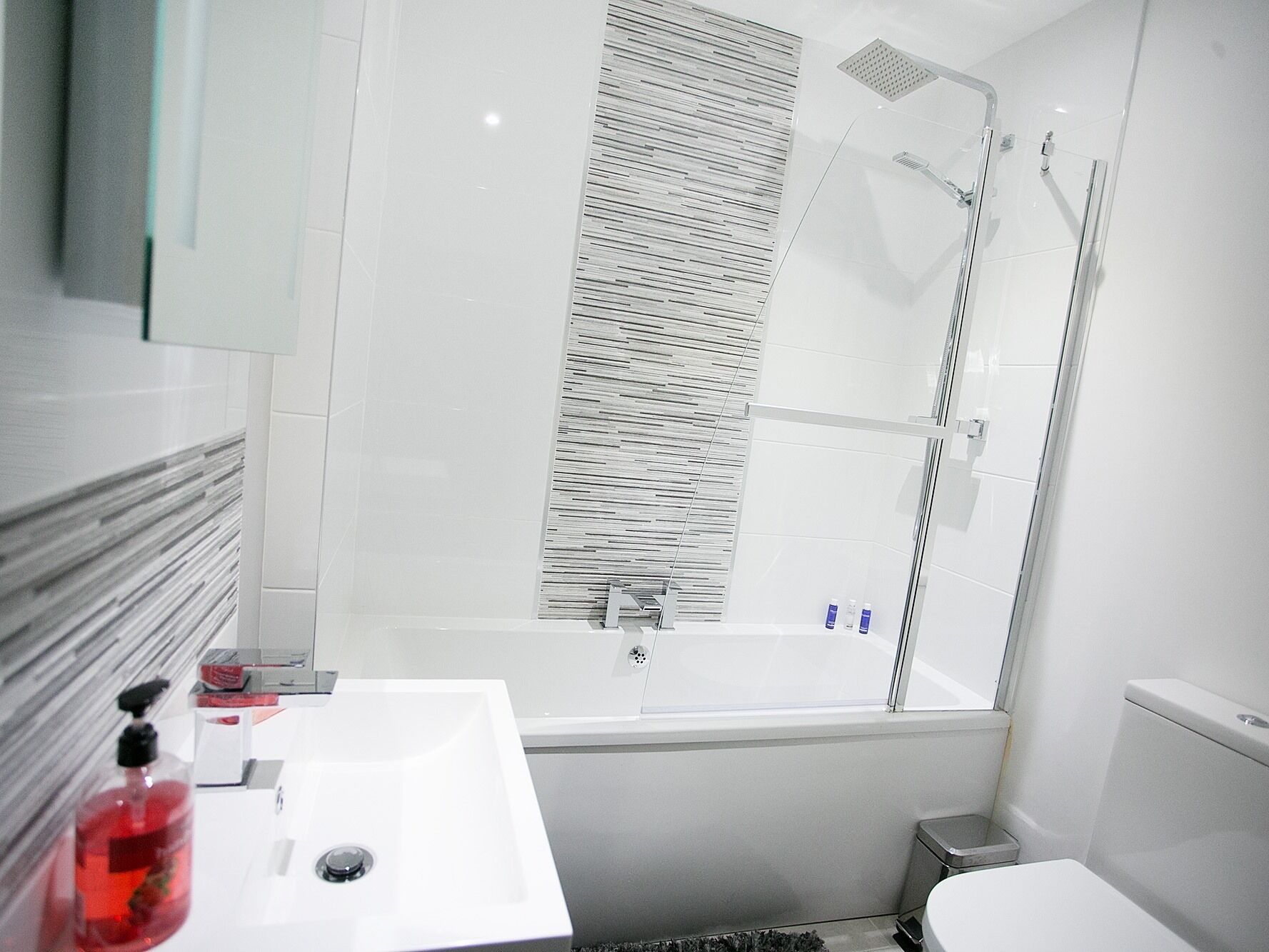 A modern bathroom with a white sink, a glass shower enclosure, and a toilet.
