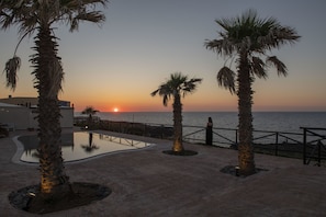 Une vue sur le coucher de soleil depuis un complexe hôtelier avec des palmiers et une piscine.
