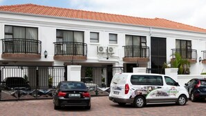 A white building with a red-tiled roof, multiple balconies, and a gated entrance. - The Shamrock Lodge (Polokwane)