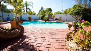 A swimming pool with a brick patio, surrounded by palm trees and potted plants. - The Shamrock Lodge (Polokwane)
