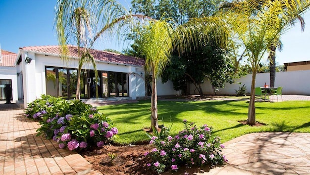 A modern house with a tiled roof, a paved driveway, and a well-maintained lawn. - The Shamrock Lodge (Polokwane)