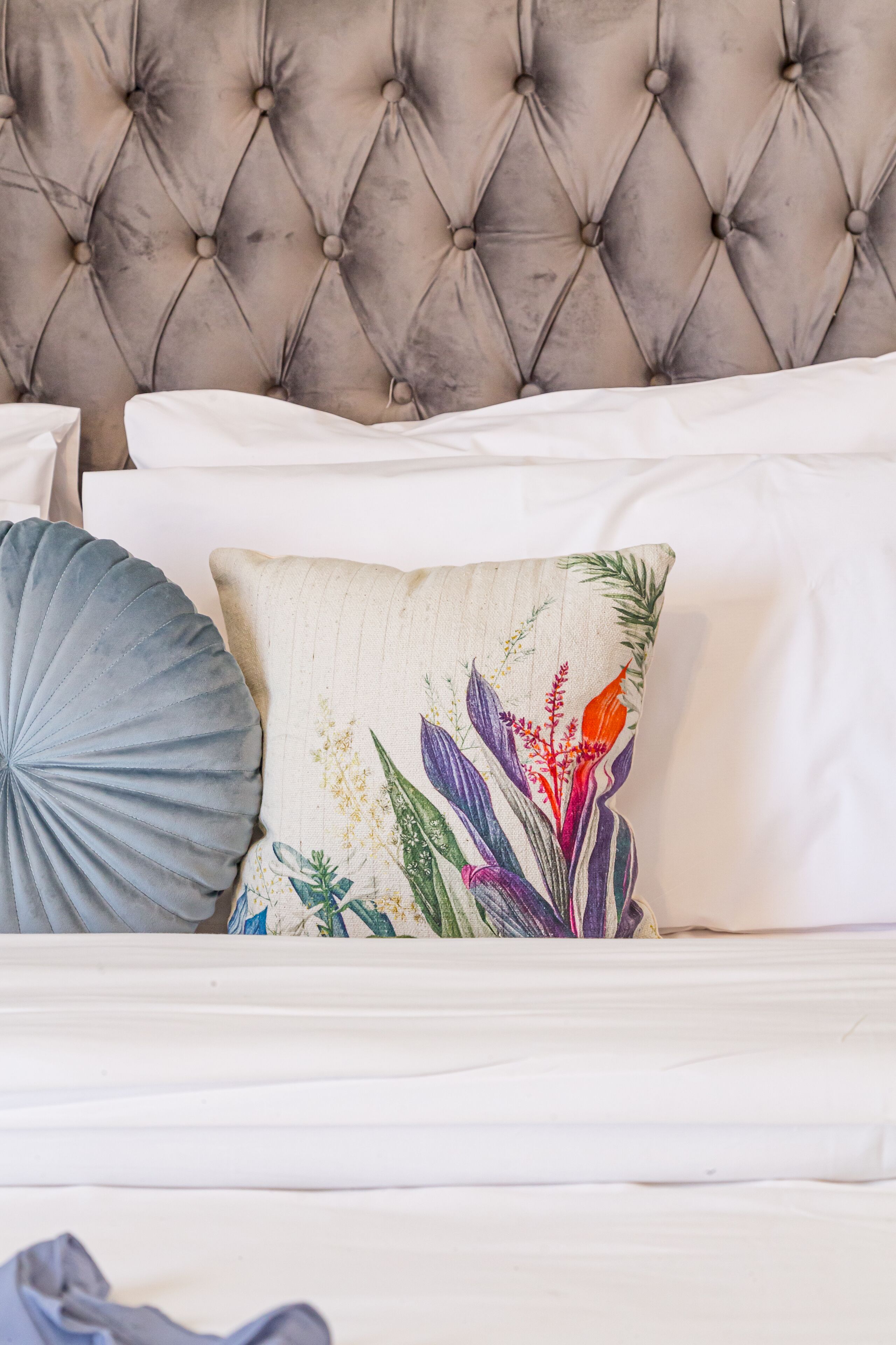 Una cama con cabecera capitonada y dos almohadas, una con diseño floral y otra con estampado de concha.