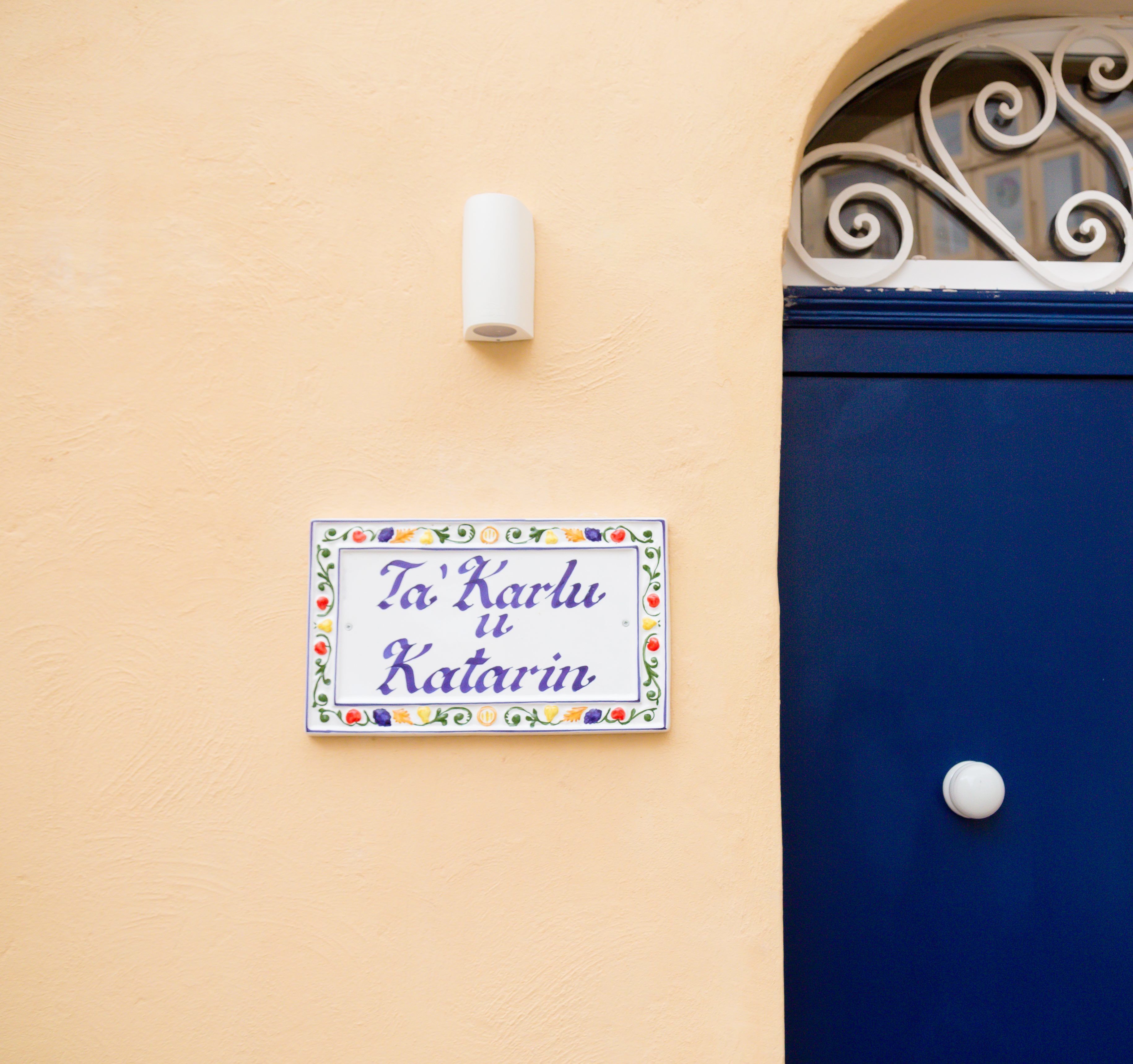 Une enseigne avec du texte dans une langue étrangère, un objet cylindrique blanc et une porte bleue ornée d’un élément décoratif en métal.