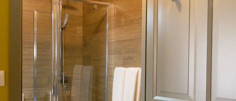 A modern bathroom with a glass-enclosed shower, wooden flooring, and a white door.