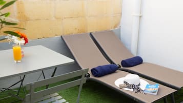Uma espreguiçadeira com uma toalha, um chapéu e um guia de viagem sobre uma mesa, junto a um copo de sumo de laranja.