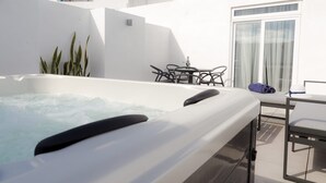 A hot tub with a table and chairs nearby, a window with curtains, and a plant. - De Rohan B&B (Zebbug)