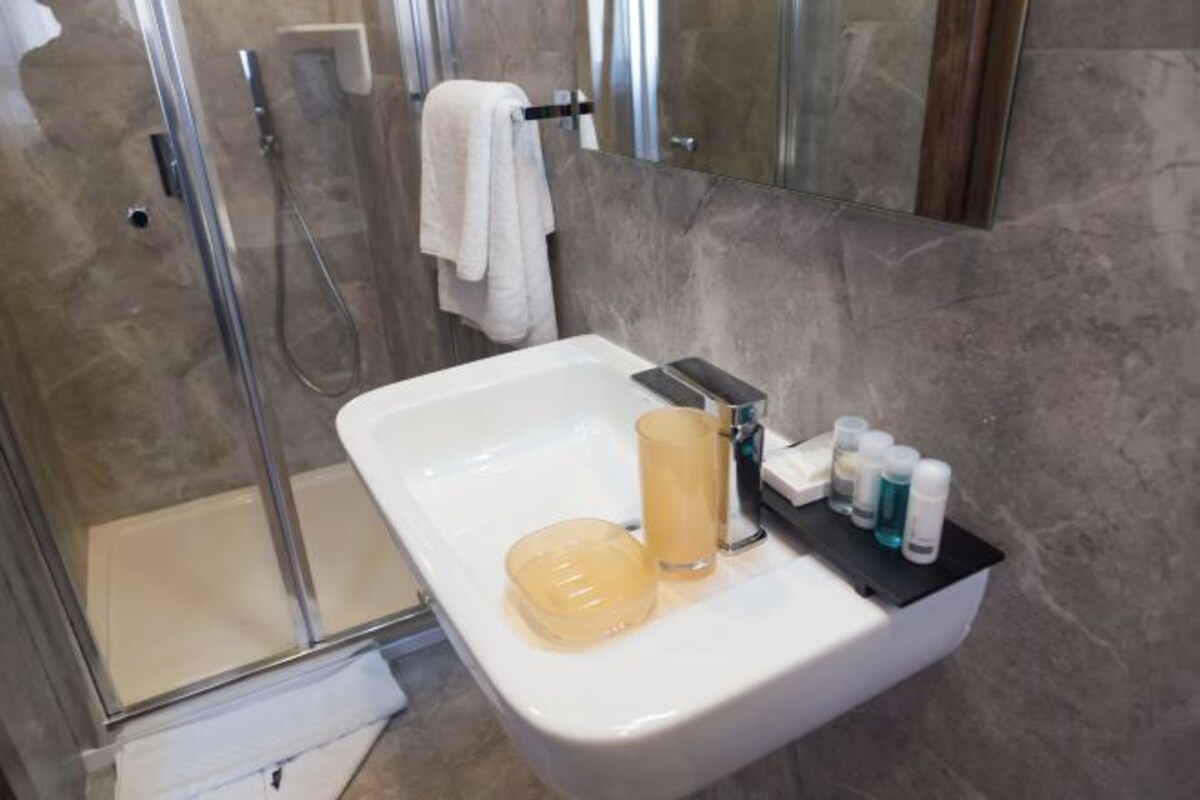 A bathroom with a glass-enclosed shower, a white sink with a soap dish, and toiletries on the sink's edge.