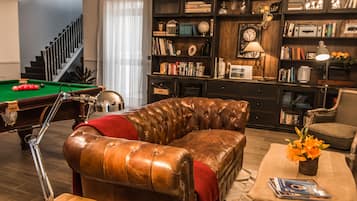 Una sala de estar con un sofá de cuero, una mesa de billar y una estantería llena de libros y objetos decorativos.