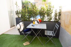 Un pequeño espacio al aire libre con una mesa y dos sillas, rodeado de plantas en macetas.