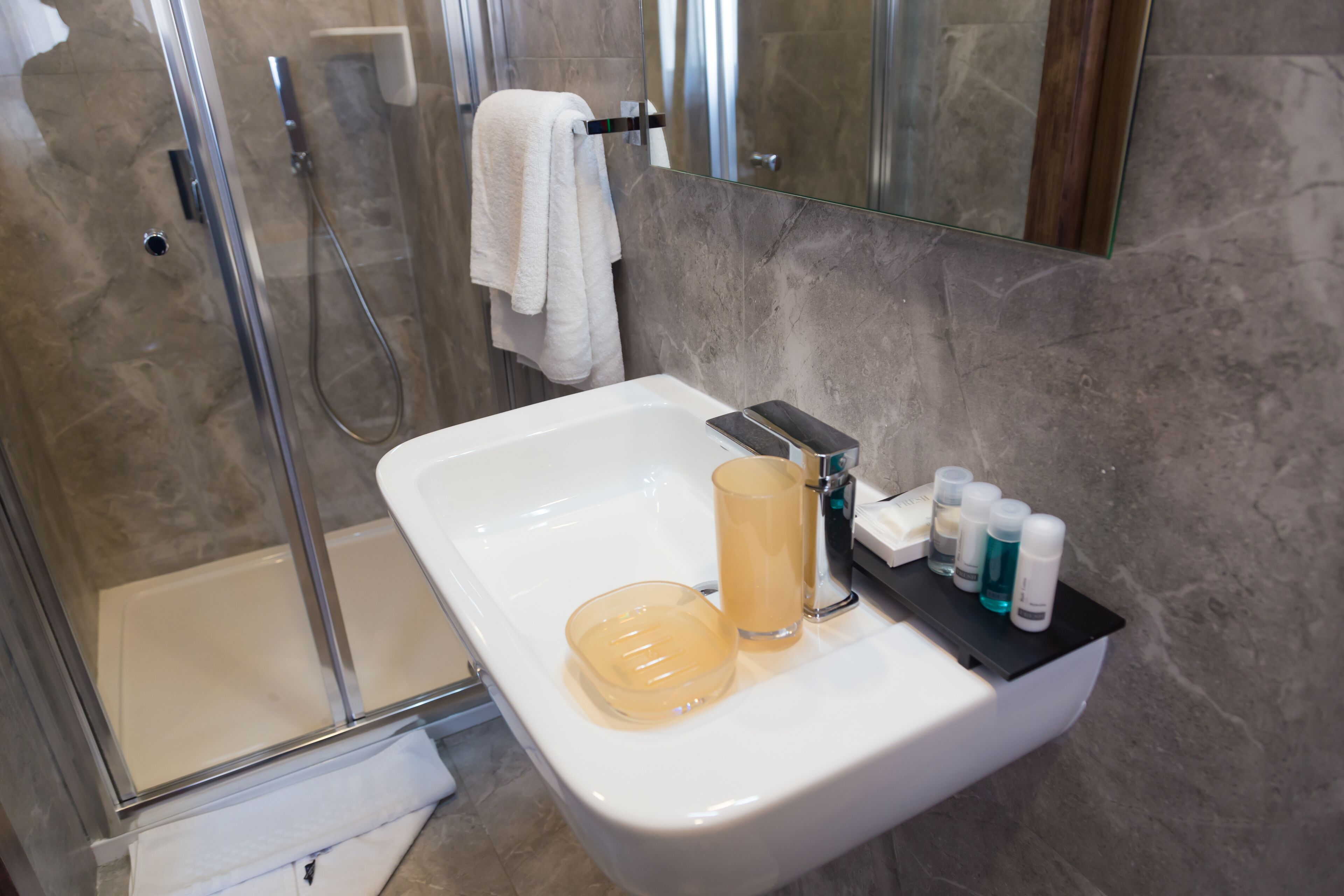 Un baño con ducha envuelta en vidrio, un lavabo blanco y un espejo encima.