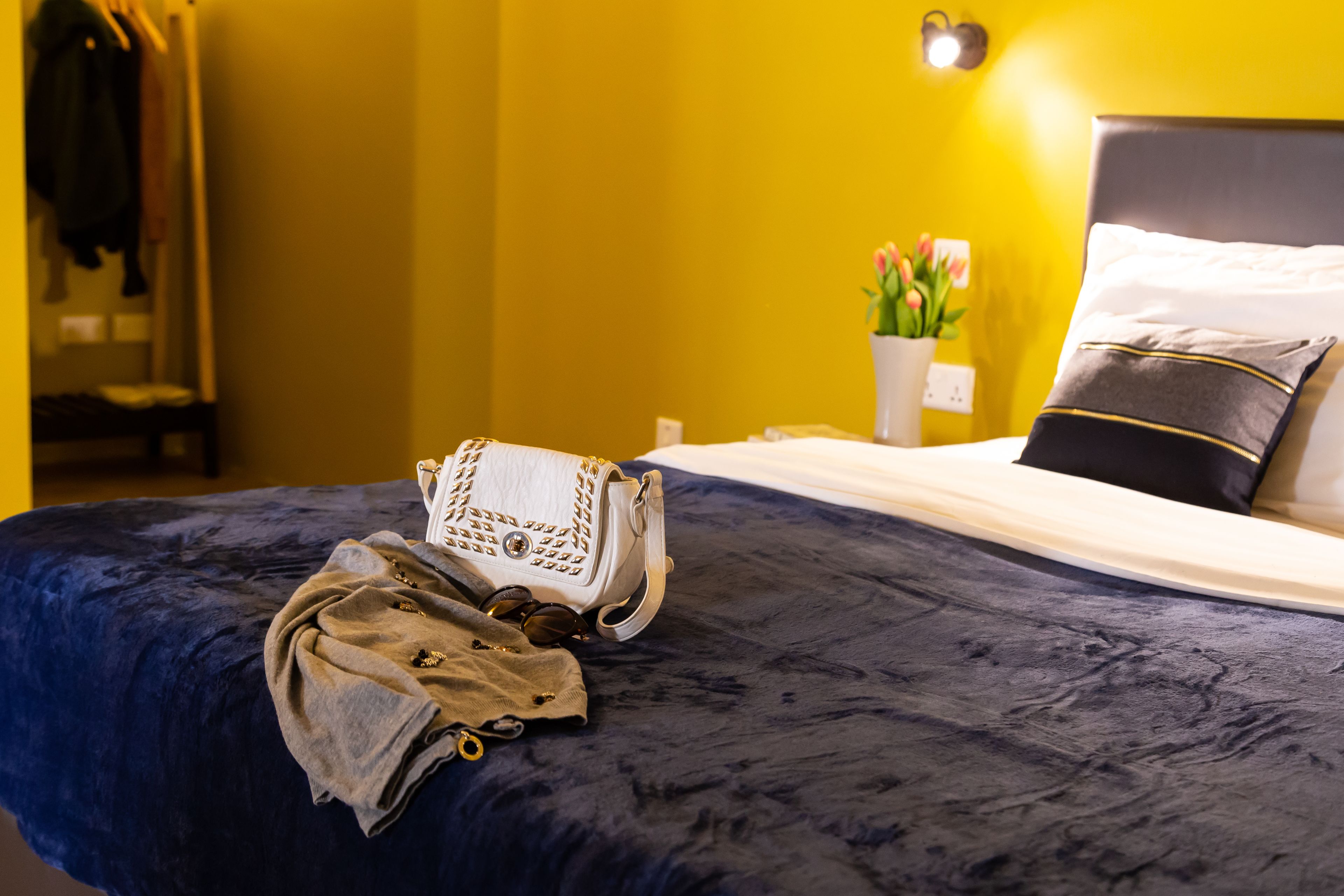A bed with a dark blue bedspread, a white handbag, and a pair of sunglasses on it.