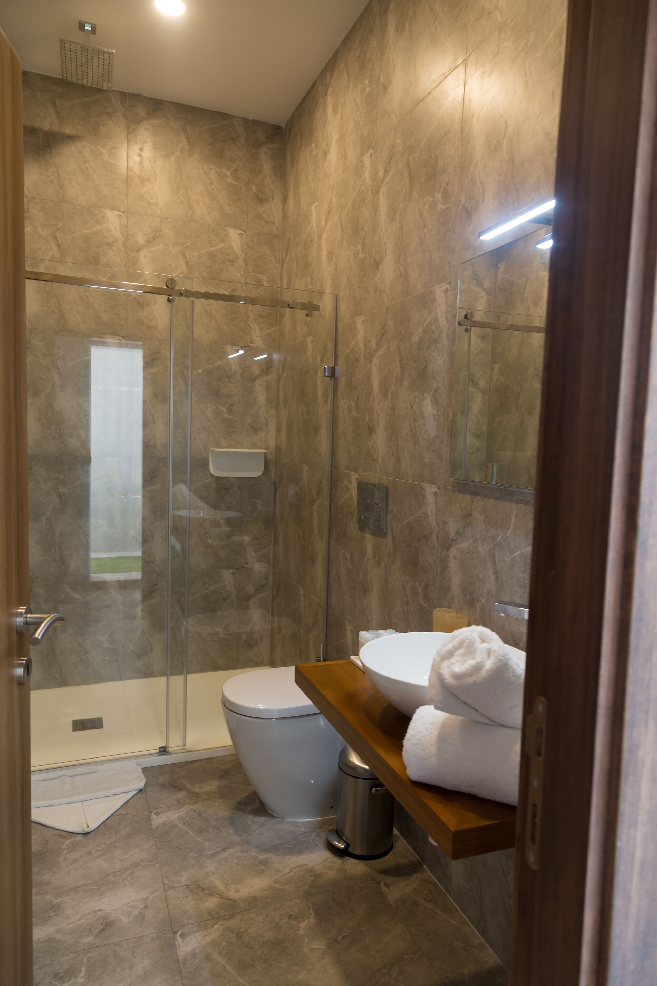 A modern bathroom with a glass-enclosed shower, a toilet, and a wooden vanity with a towel rack.