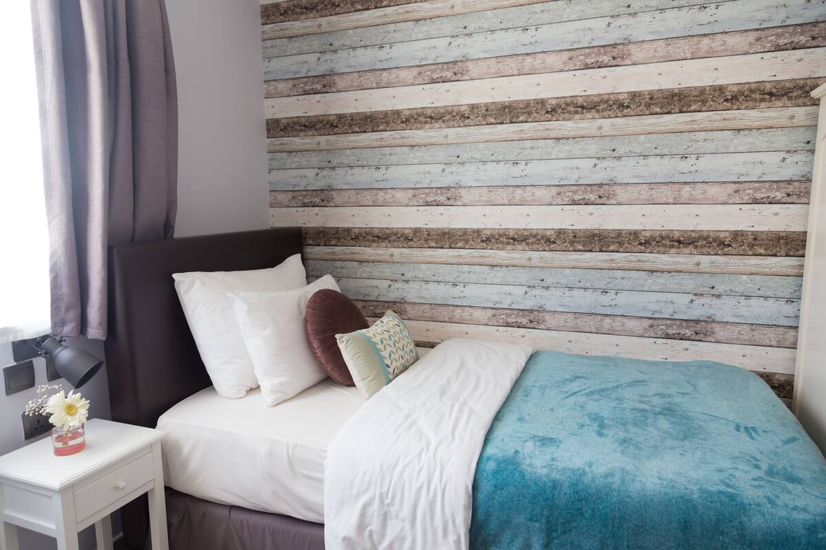 Un lit bien fait, avec une literie blanche et bleue, une tête de lit sombre et un mur en bois composé de planches horizontales.