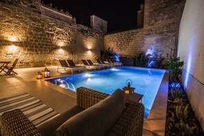 Une piscine avec des chaises longues et un mur en pierre.