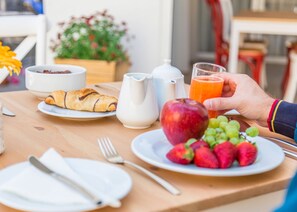 A breakfast table with croissants, a pitcher, a glass of orange juice, and a plate of strawberries and grapes.