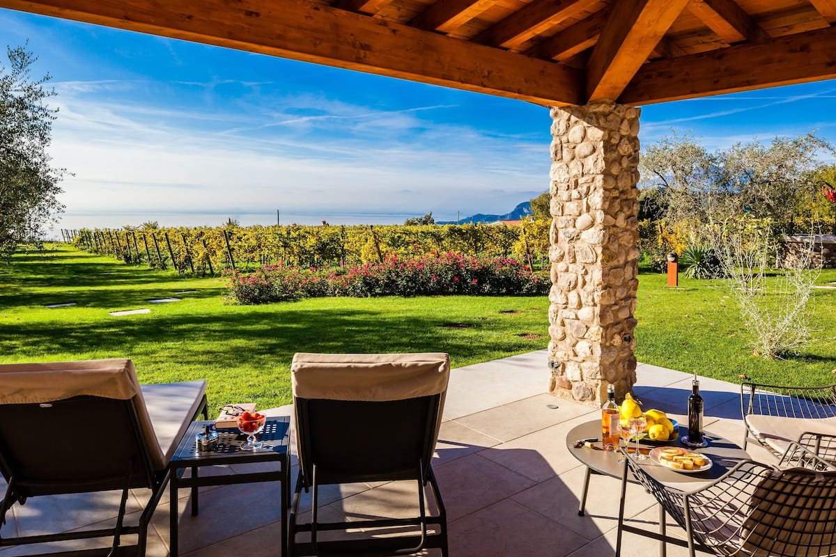 Eine Terrasse im Freien mit Steinsäulen, einem Tisch und Stühlen sowie Blick auf einen Weinberg.