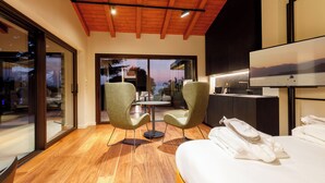 Une chambre d’hôtel moderne avec un plafond en bois, un grand lit, deux fauteuils, une table à manger et une vue sur l’extérieur.