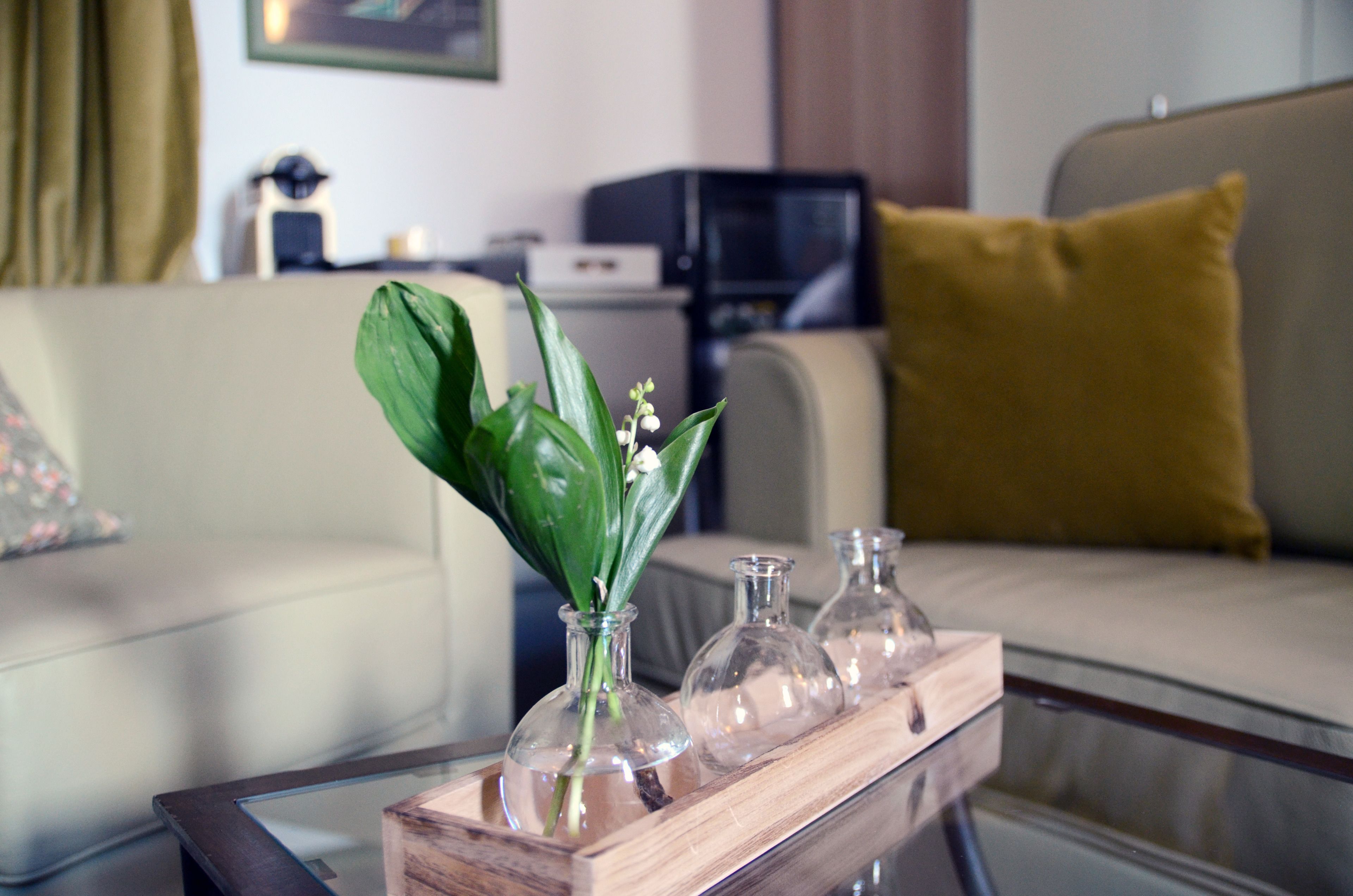 Sala de estar com mesa de centro de vidro, onde se vê um vaso com folhas verdes e flores brancas.