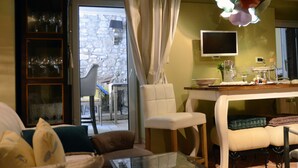 A cozy living room with a sofa, a dining table with chairs, a TV, and a stone wall. - Villa Orh (Rovinj)