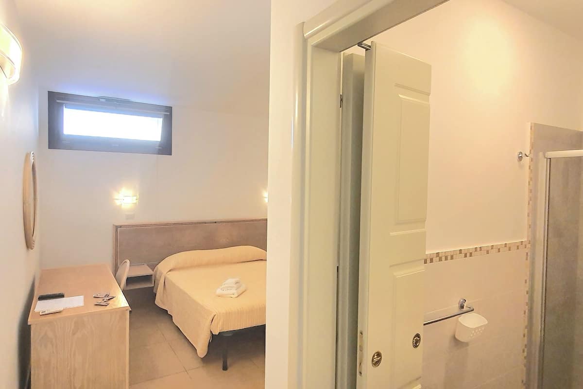 Une chambre d’hôtel comprenant un lit, un bureau, une chaise, une table de chevet, une commode, un téléviseur fixé au mur et une salle de bain avec douche et toilettes.