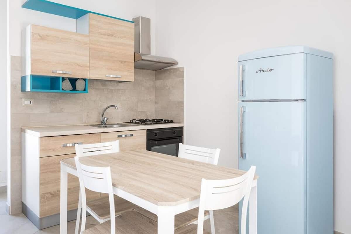 Une cuisine compacte avec une table et des chaises en bois, une cuisinière encastrée et un réfrigérateur bleu clair.