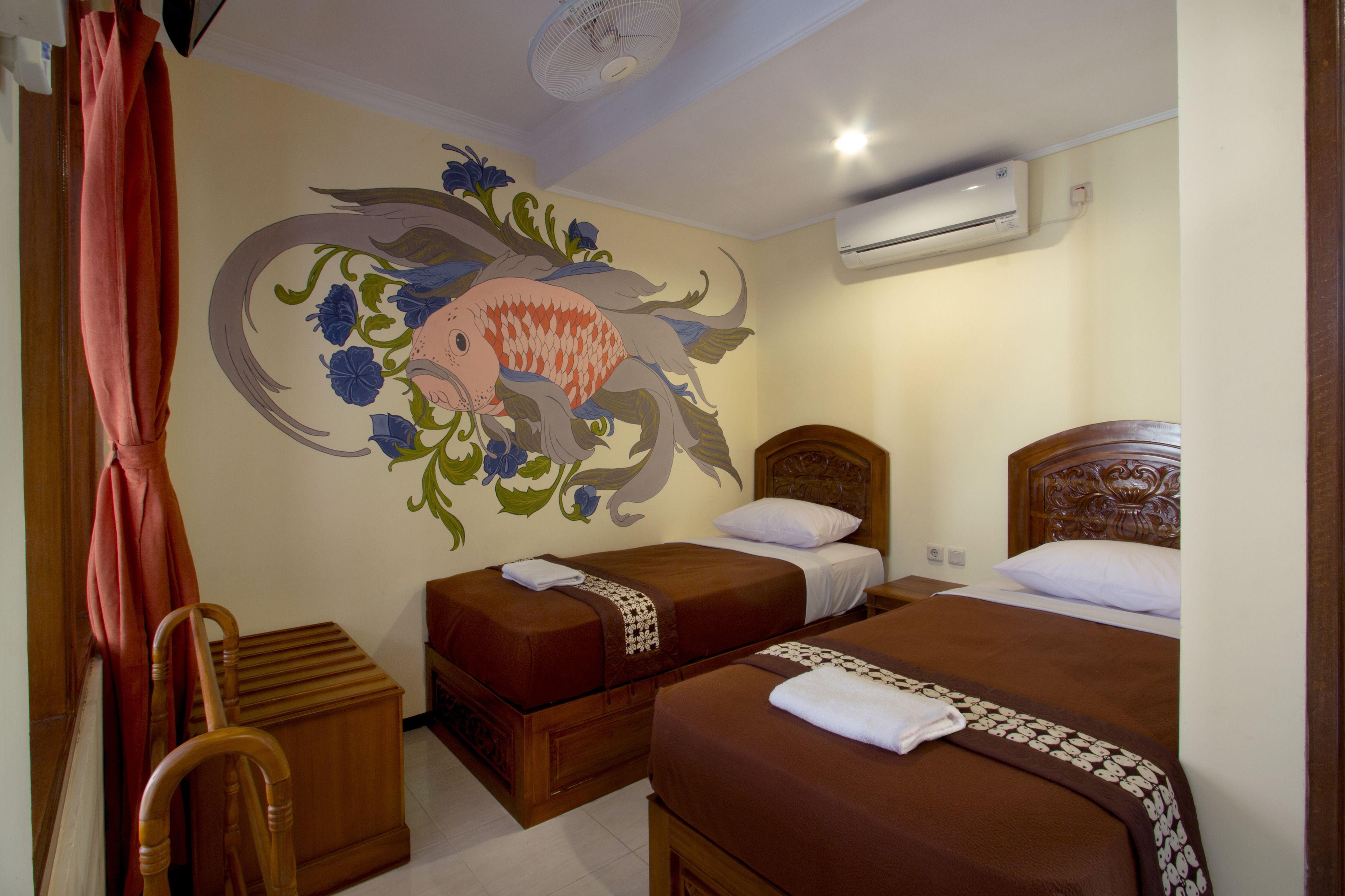Habitación de hotel con dos camas individuales, una silla de madera, aire acondicionado de pared y un mural decorativo con peces.