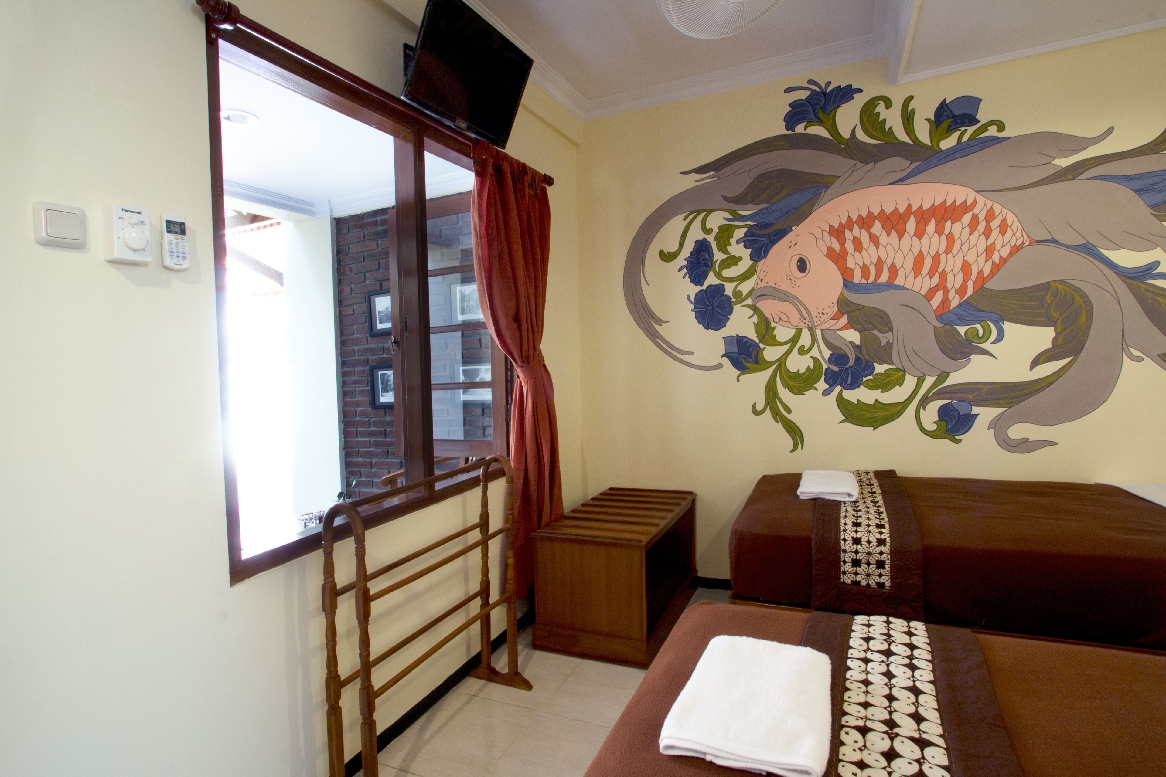 A hotel room with a bed, a small wooden bench, a wall-mounted TV, and a window with curtains.