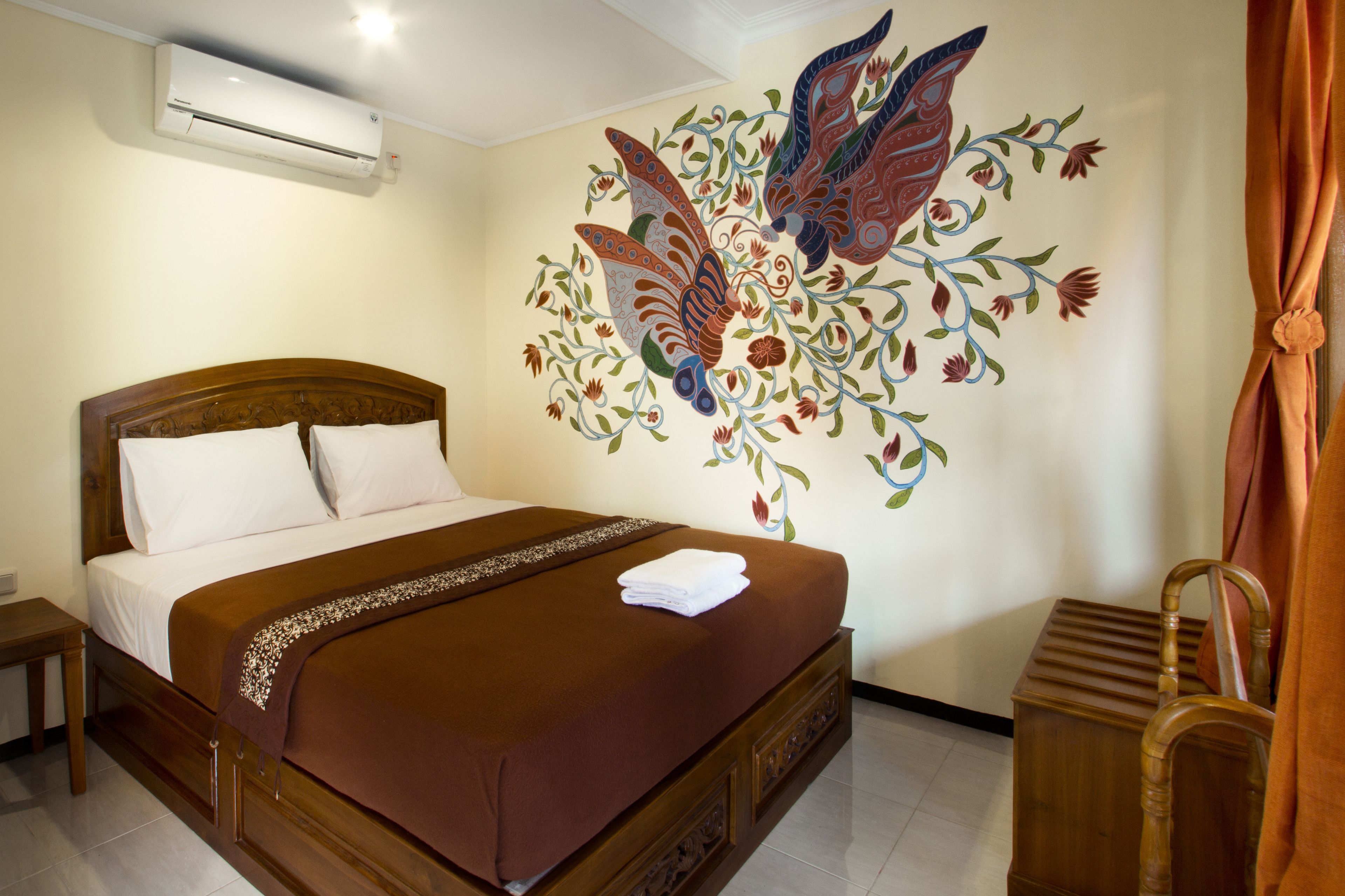 A hotel room with a wooden bed, a decorative wall mural, and a wooden chair.