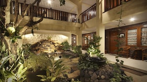 Un jardín interior de varios niveles con una cascada de piedra, plantas en macetas y una zona de estar con mobiliario de madera.