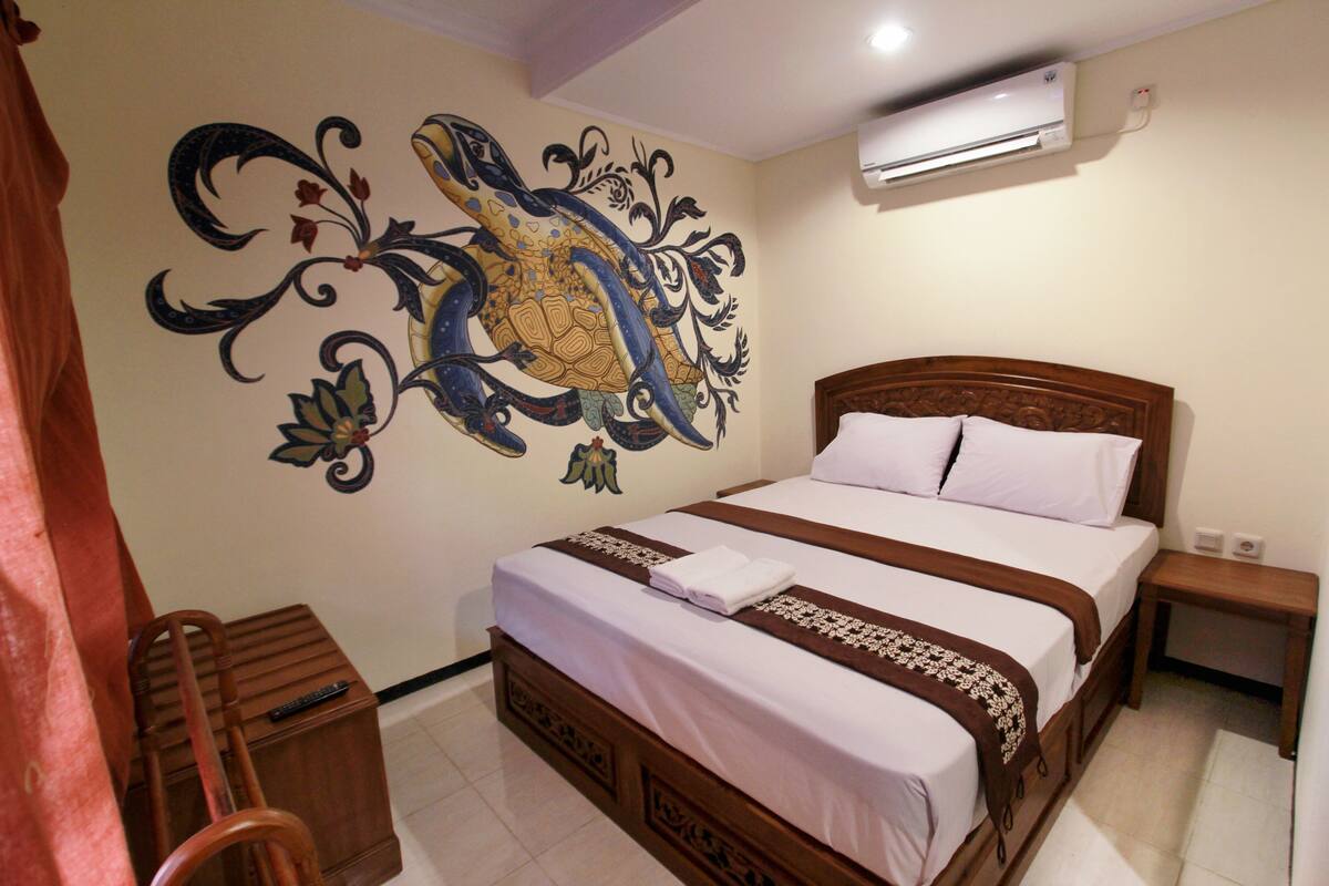 A bedroom with a large bed, a wooden nightstand, a small wooden chair, and a wall mural.
