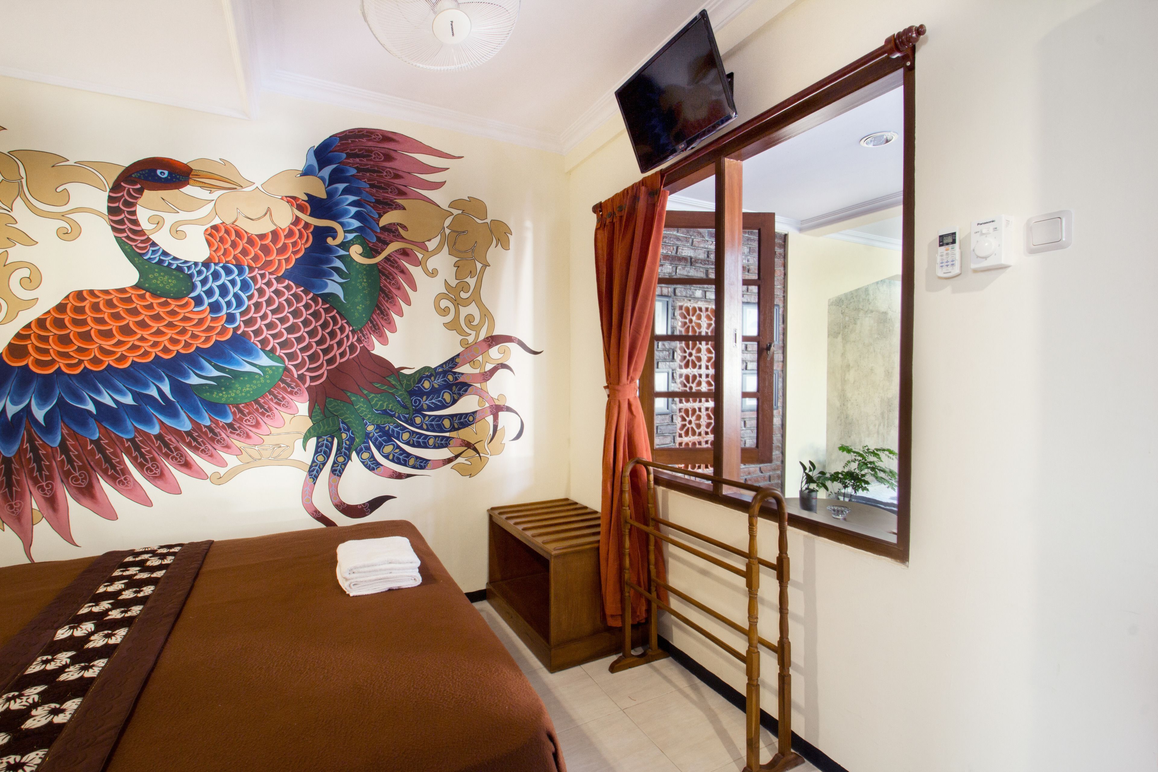 A room with a bed, a wall mural, a television, and a window with curtains.
