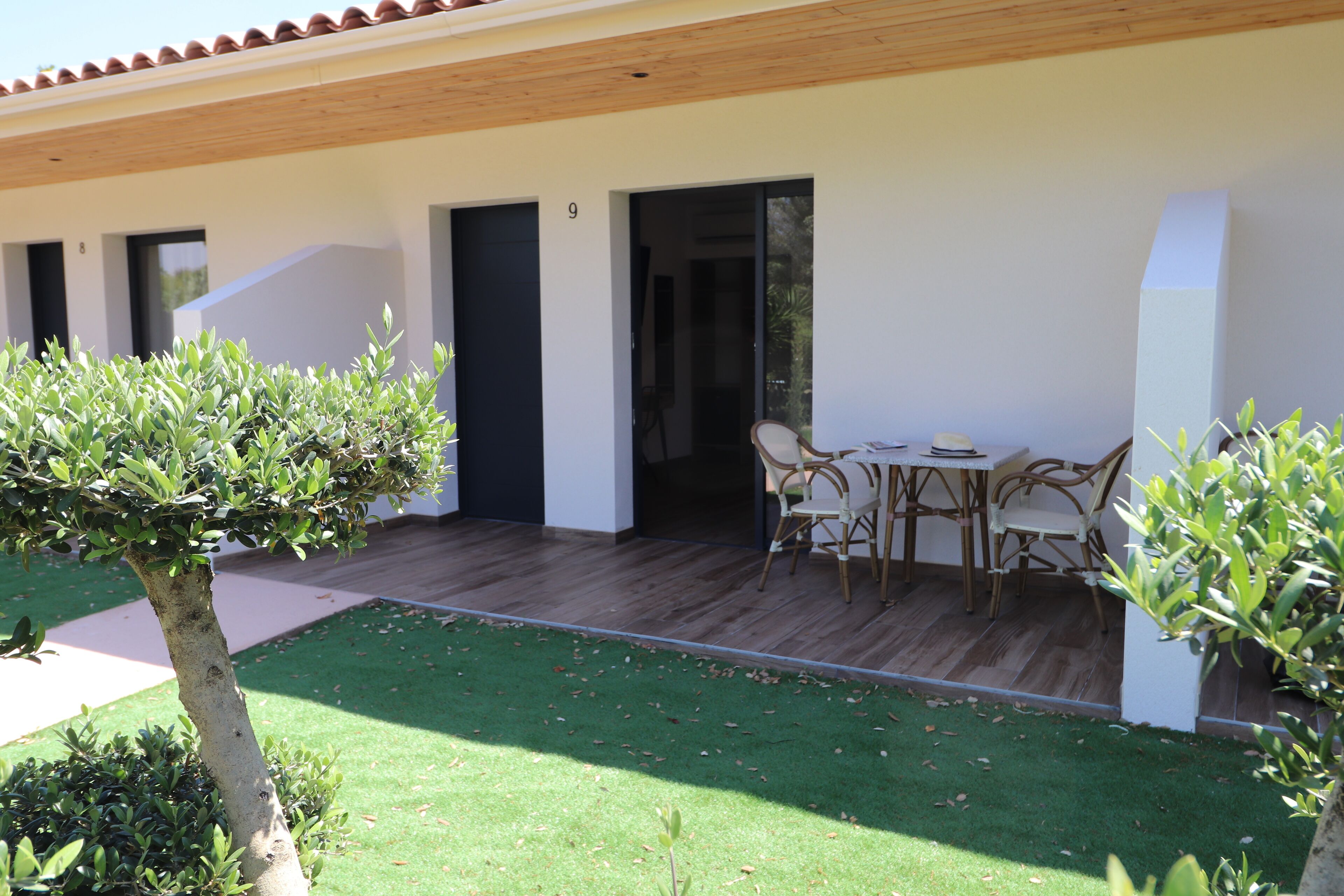 A modern building with a patio area featuring a table and chairs, surrounded by greenery and a well-maintained lawn.