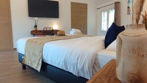 A modern bedroom with a large bed, a flat-screen TV mounted on the wall, and a wooden floor. - Hôtel Padolo (Bonifacio)