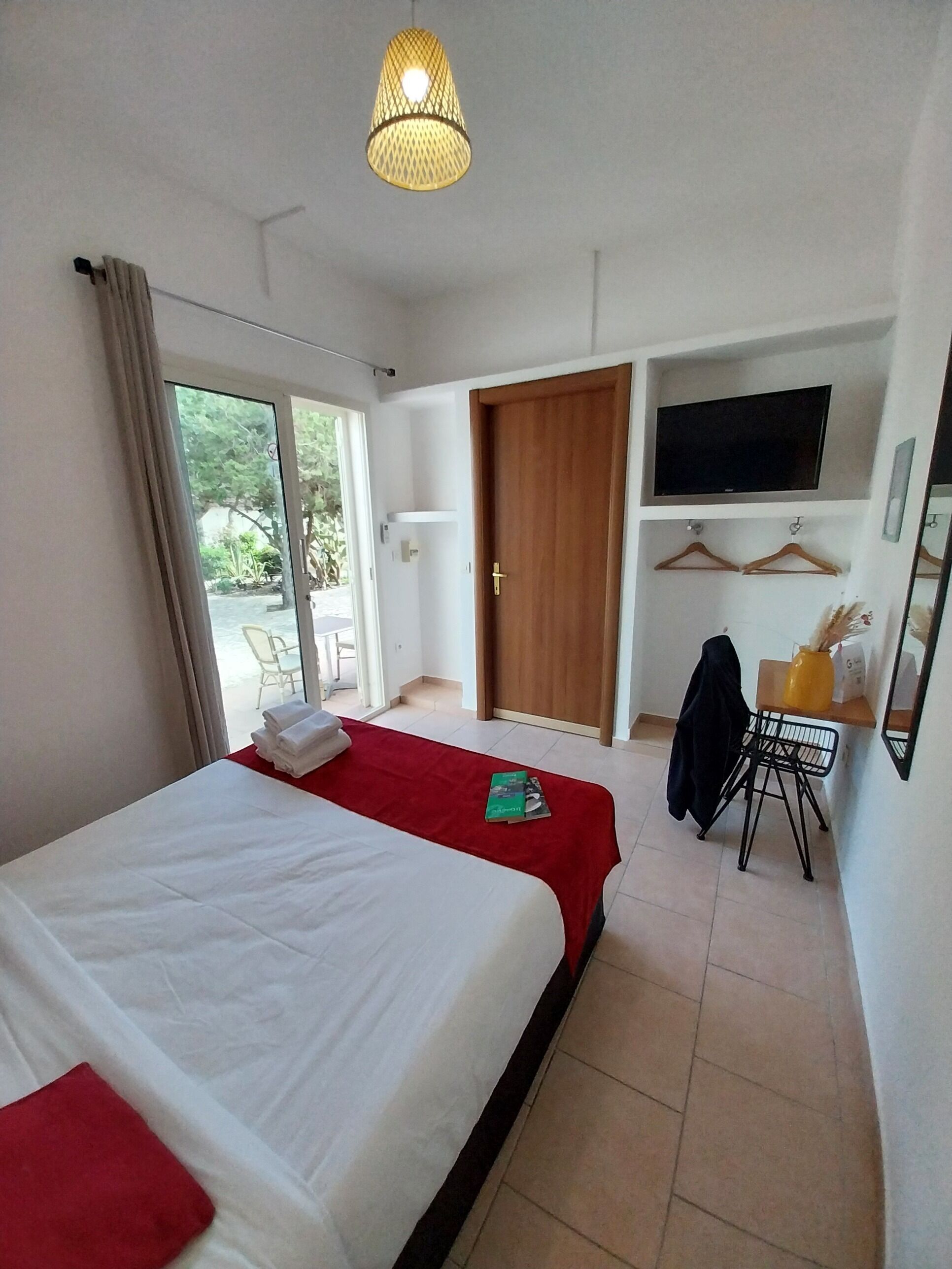 Habitación de hotel con cama, televisión, escritorio con silla y puerta corrediza a un balcón.