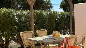Une terrasse extérieure avec une table et des chaises, une pergola en bois et une végétation luxuriante en arrière-plan.