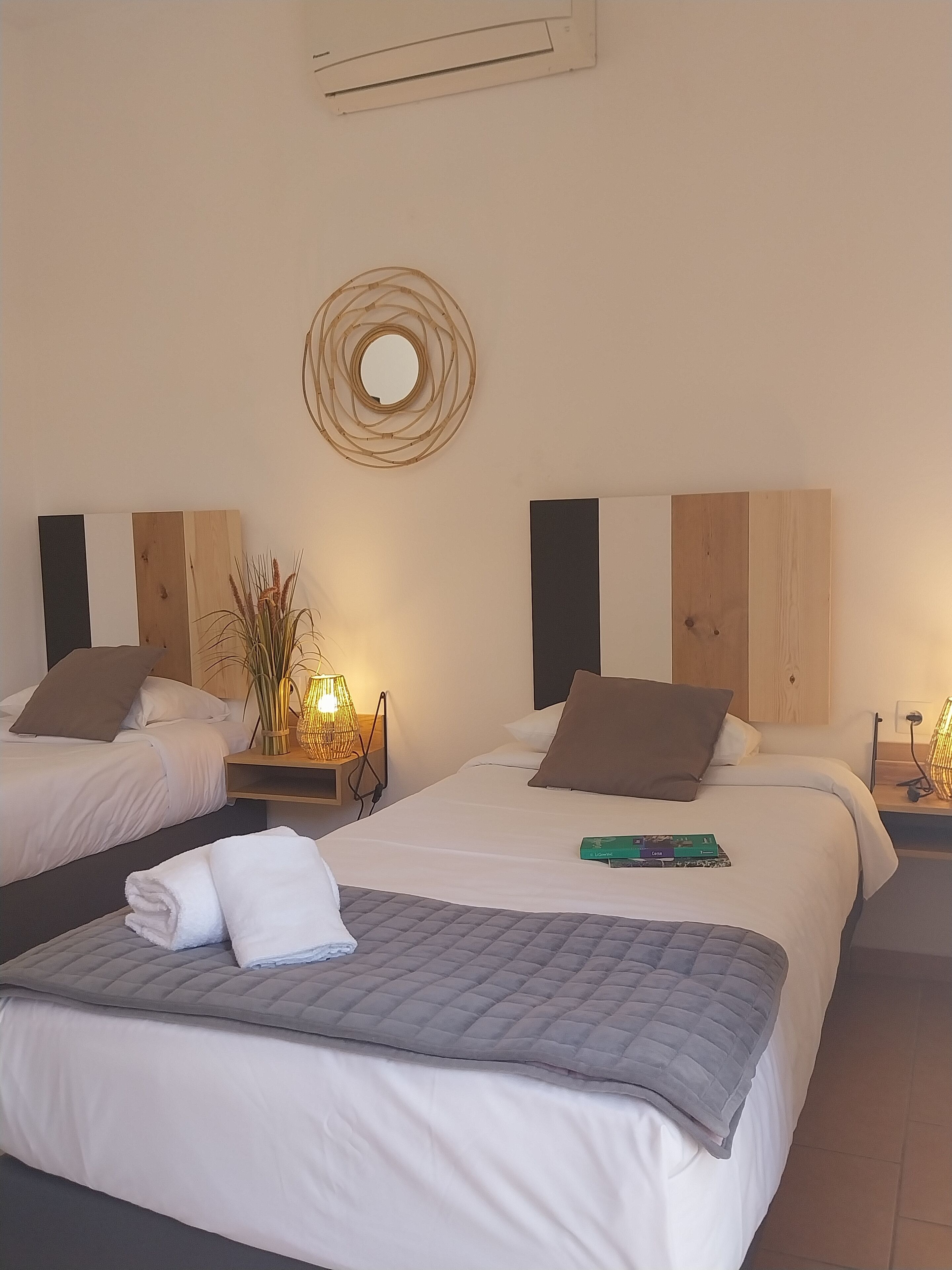 Una habitación de hotel con dos camas, un espejo redondo y una mesita de noche con una lámpara.