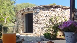 A stone building with a door, a table with a plate of croissants, a glass of orange juice, and a potted plant labeled "FLOWERS & GARDEN". - Hôtel Padolo (Bonifacio)