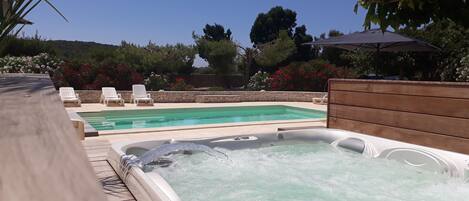 A hot tub and a swimming pool with lounge chairs and a stone wall.