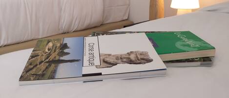 A neatly made bed with white bedding, a black pillow, and a bedside table with a lamp and a vase with dried flowers.