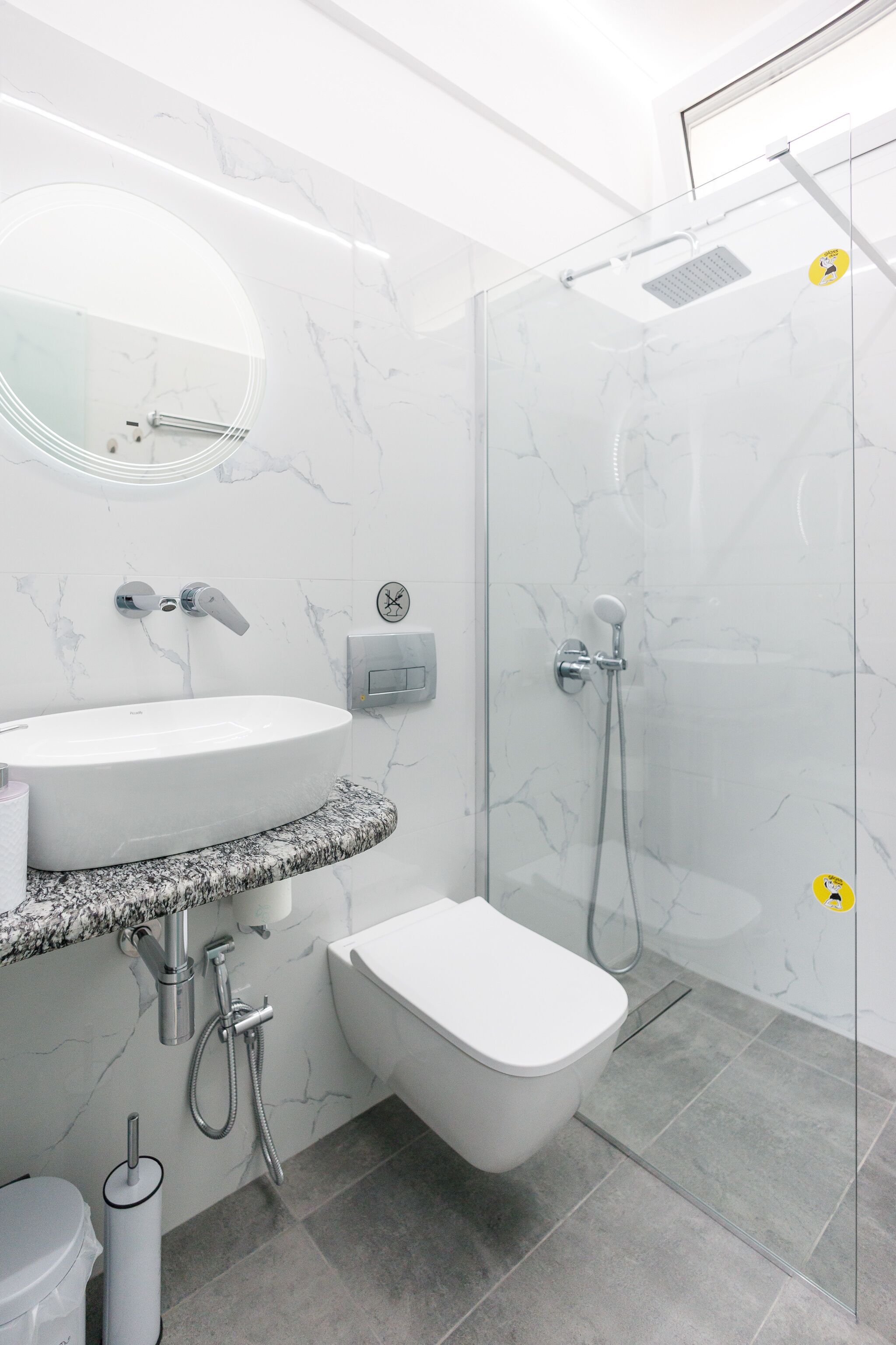 Een moderne badkamer met een douchecabine van glas, een witte wastafel met een marmeren blad en een toilet.