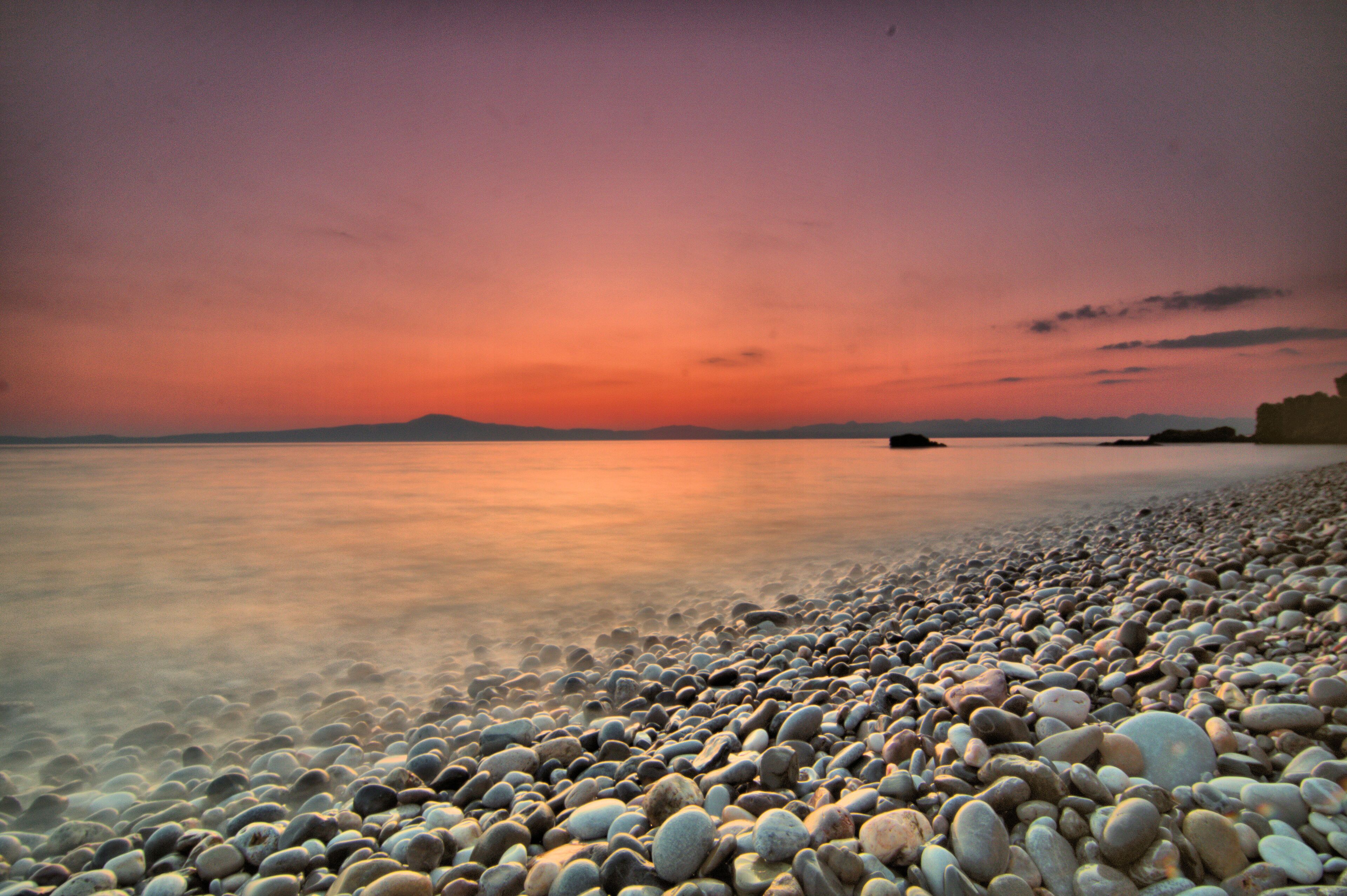 Una playa de guijarros con un mar tranquilo y un cielo al atardecer.