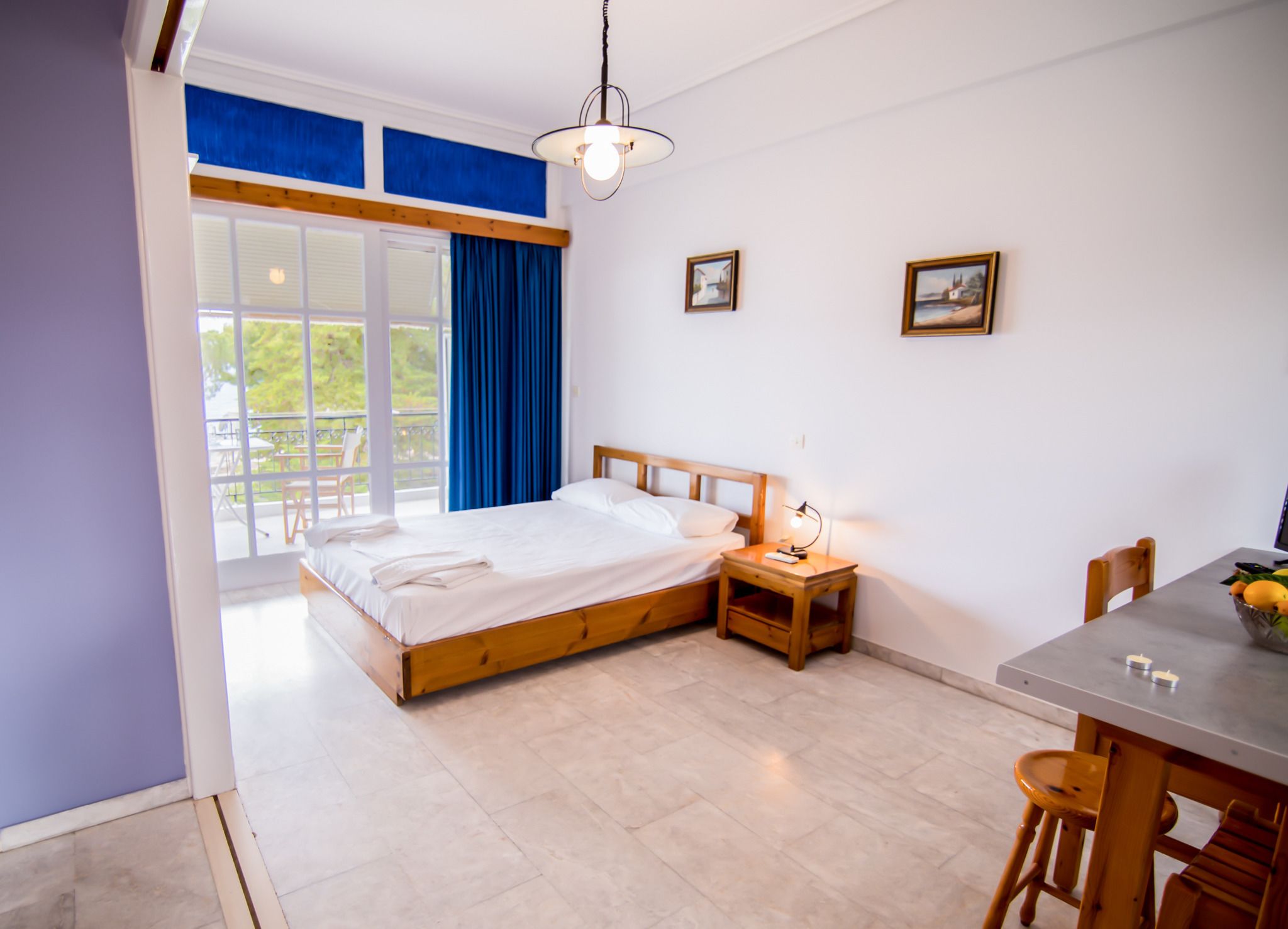 Un dormitorio con cama, mesita de noche, lámpara y una zona de comedor con mesa y sillas.