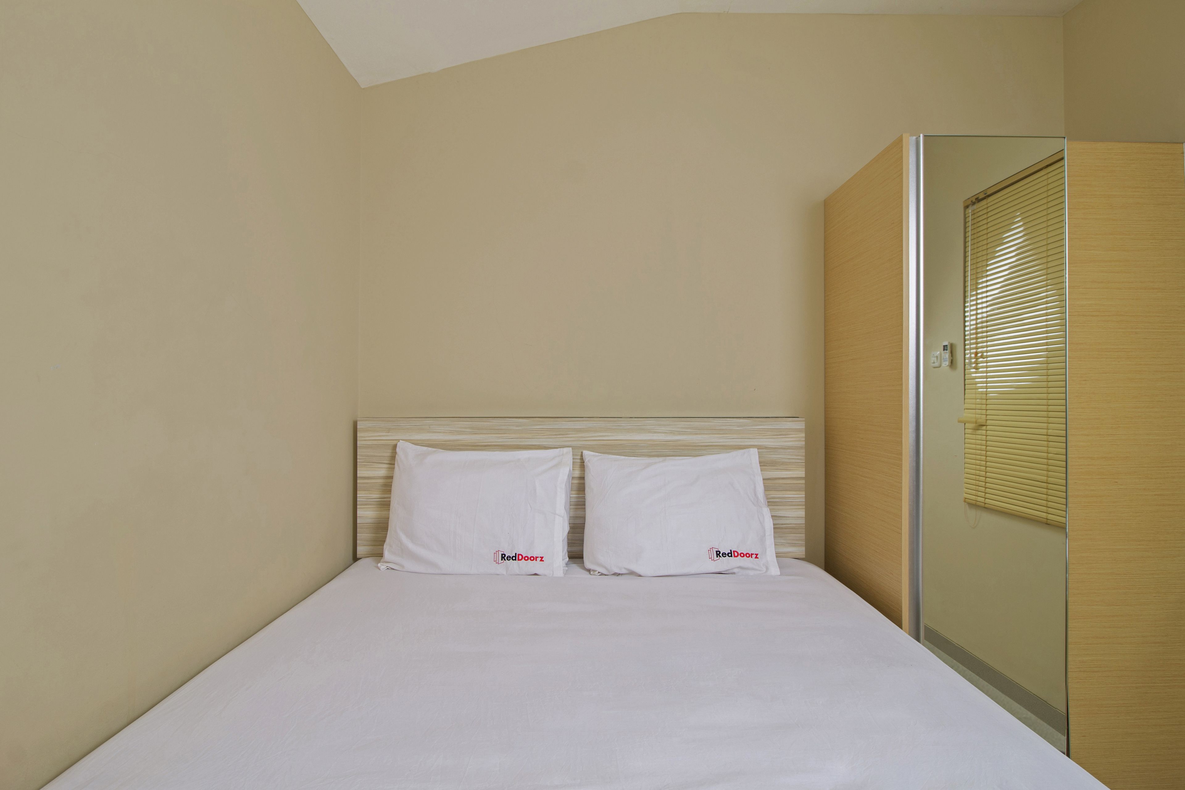 A neatly made bed with white linens and pillows, a wooden headboard, and a glass shower enclosure.
