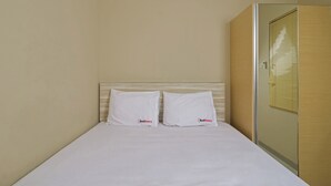 A neatly made bed with white linens and pillows, a wooden headboard, and a glass shower enclosure. - RedDoorz Plus @ Setiabudi Tengah (Jakarta)